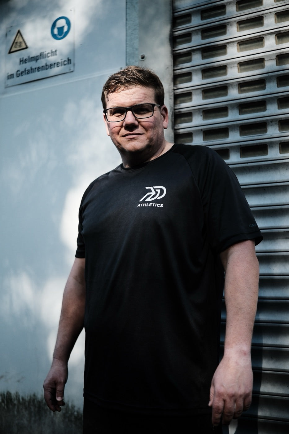 Athlet im schwarzen PGO-Athletics-Shirt vor einer Industriehalle