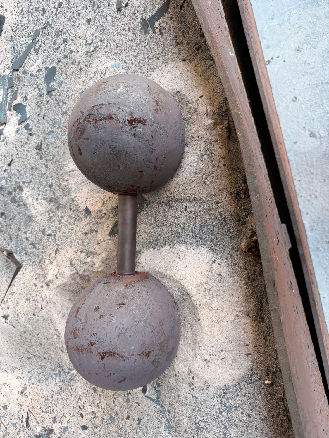 Fertig geschmiedete Kugelhantel von PGO Athletics mit Zunder und Hammerspuren, im Sand der Schmiede von oben