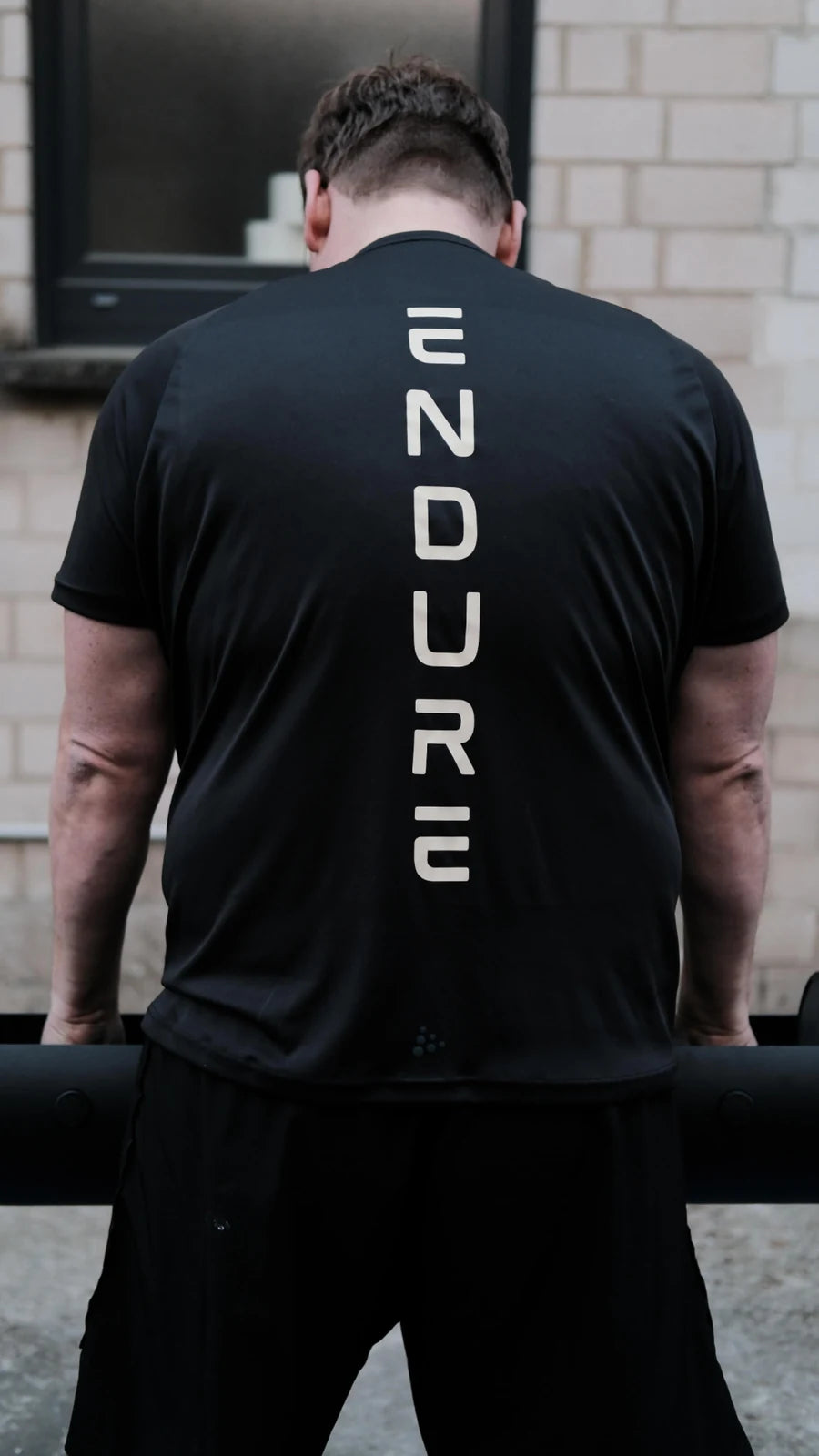 Athlet von hinten an der Langhantel, auf dem Rücken seines schwarzen Shirts der senkrechte Schriftzug ENDURE